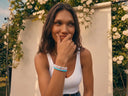 A woman wearing a stack of colourful gemstone bracelets outdoors in front of a white backdrop