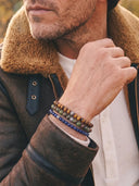 A person wearing a shearling jacket and a stack of Deep Blue, Bloodstone and Tigers Eye bracelets.