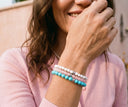 A woman smiling candidly and wearing a stack of our best selling gemstone bracelets