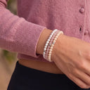 A close-up of a person wearing a stack of Snow, Rose Quartz and Ivory 4mm beaded bracelets.