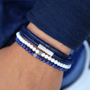 Close-up of a wrist wearing multiple blue and white beaded bracelets