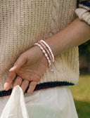 A hand wearing a stack of white and pink beaded bracelets
