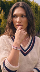 A woman wearing a cream knit V-neck sweater with navy and burgundy stripes, accessorised with a pearl necklace and gemstone beaded bracelets