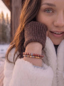 A woman in a white fur coat outdoors in the snow wearing Sedona Jasper and Yellow Ochre bracelets.