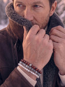 A close-up lifestyle shot of a man wearing a stack of beaded bracelets on his wrist, while pulling up a shearling jacket.