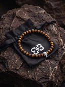 A tigers eye beaded bracelet with a 925 sterling silver skull on a textured rock background.