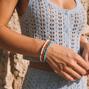 A woman wearing Snow, Burnt Orange and Turquoise bracelets at the beach