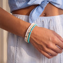 A close-up of a wrist wearing Snow, Ivory and Turquoise beaded bracelets