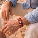 A close-up of a person wearing a Chocolate Brown Leather bracelet paired with Tiger Eye and Burnt Orange beaded bracelets