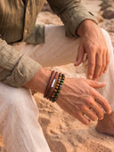 A man on a beach wearing a Chocolate Leather Bracelet with Tigers Eye beaded bracelets