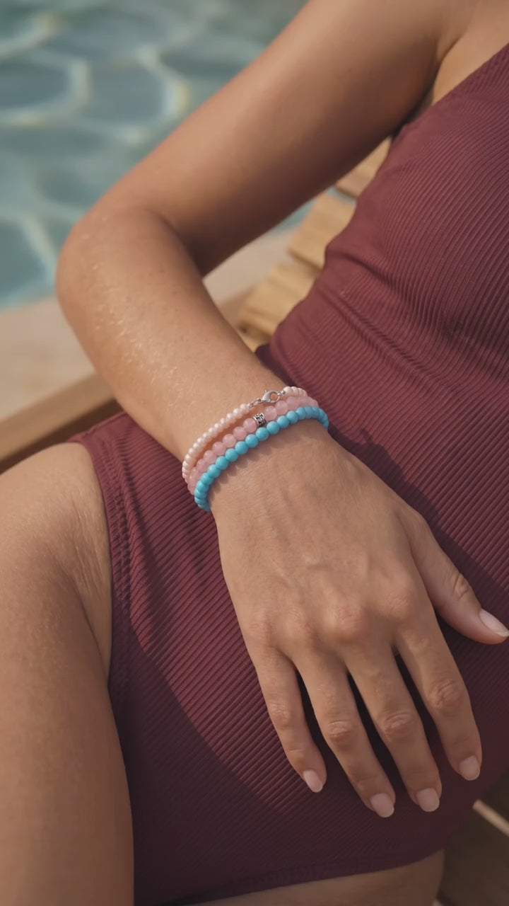 A woman sunbathing poolside wearing Pearls with Rose Quartz and Turquoise bracelets